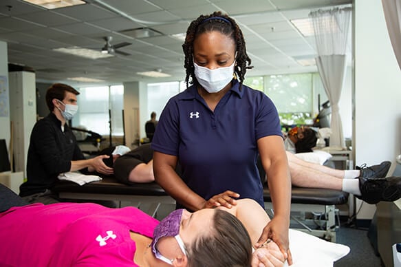 Young female therapist wearing face mask working on a patient's arm on a therapy table.