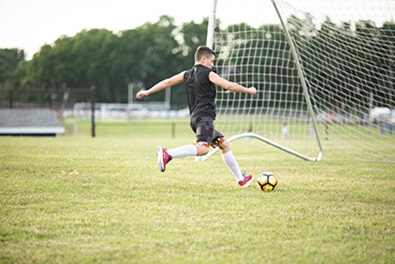 Young boy kicking soccer ball into net on field
