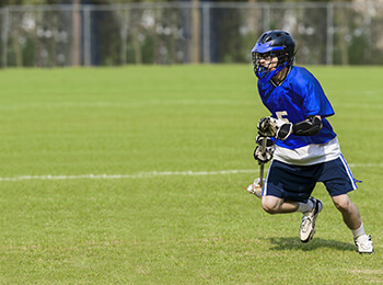 A male student running on a field, playing lacrosse.